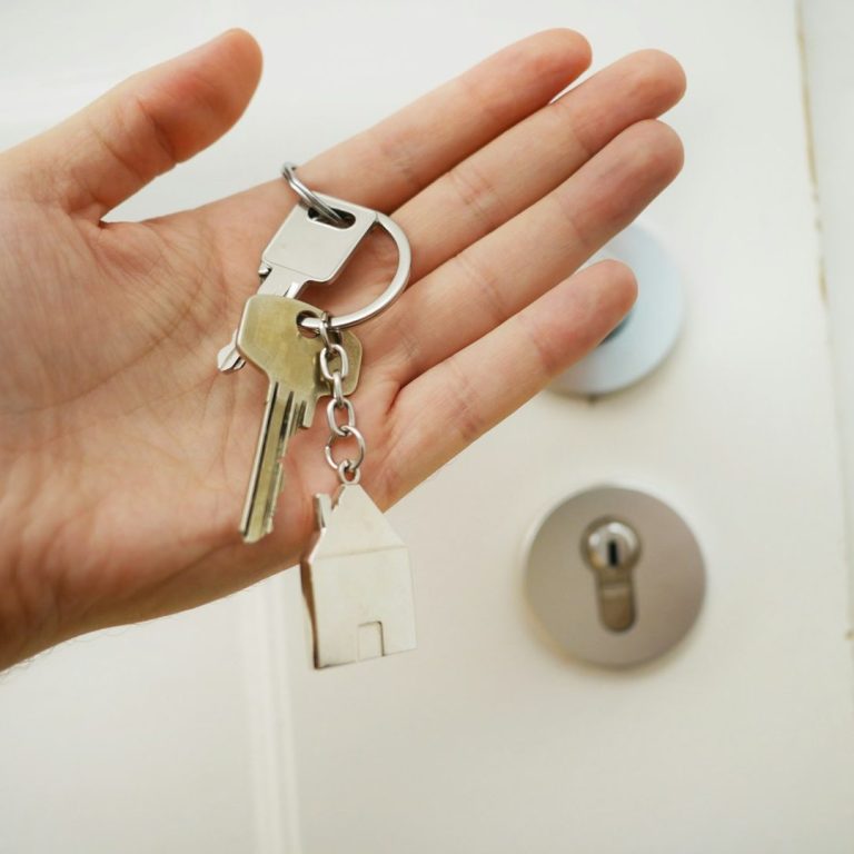 Eine Hand hält Schlüssel, darunter ein kleiner Schlüsselanhänger in Form eines Hauses.